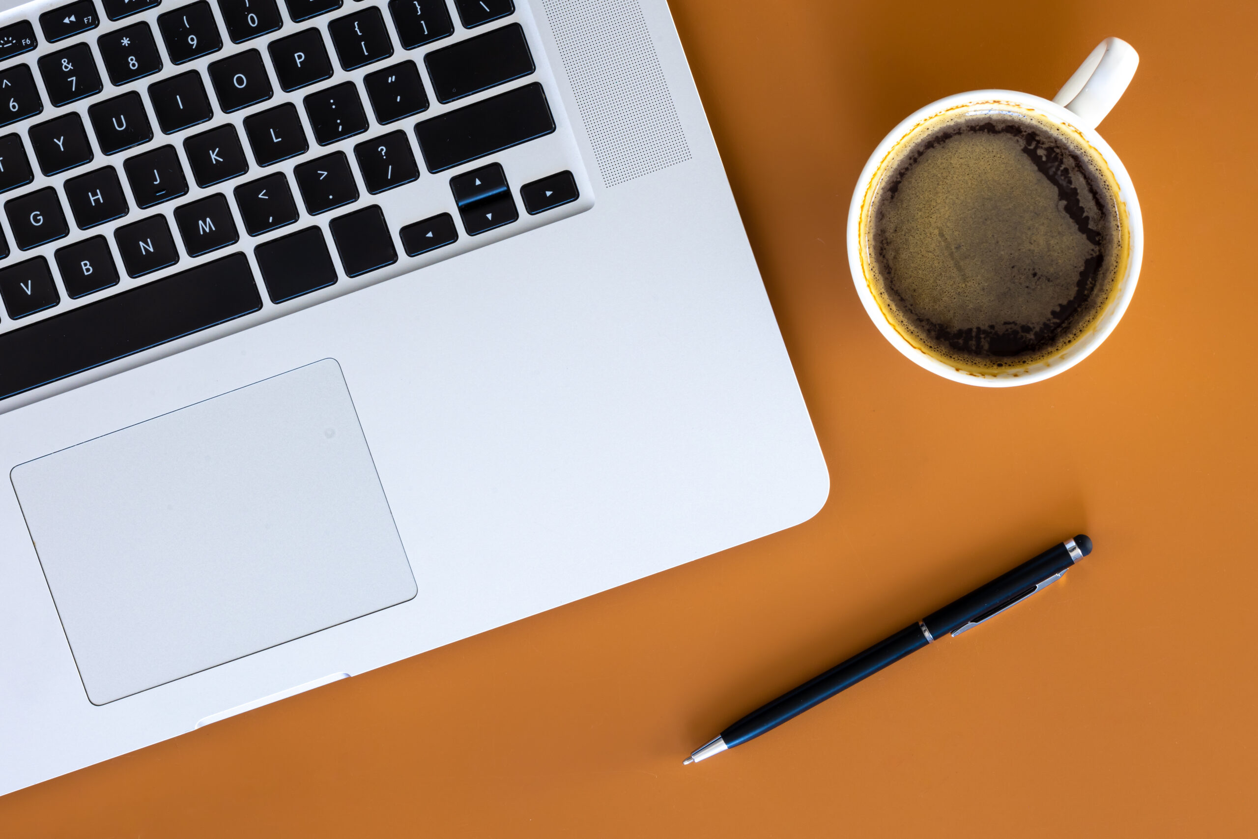 Portátil, taza de café y bolígrafo sobre un escritorio naranja